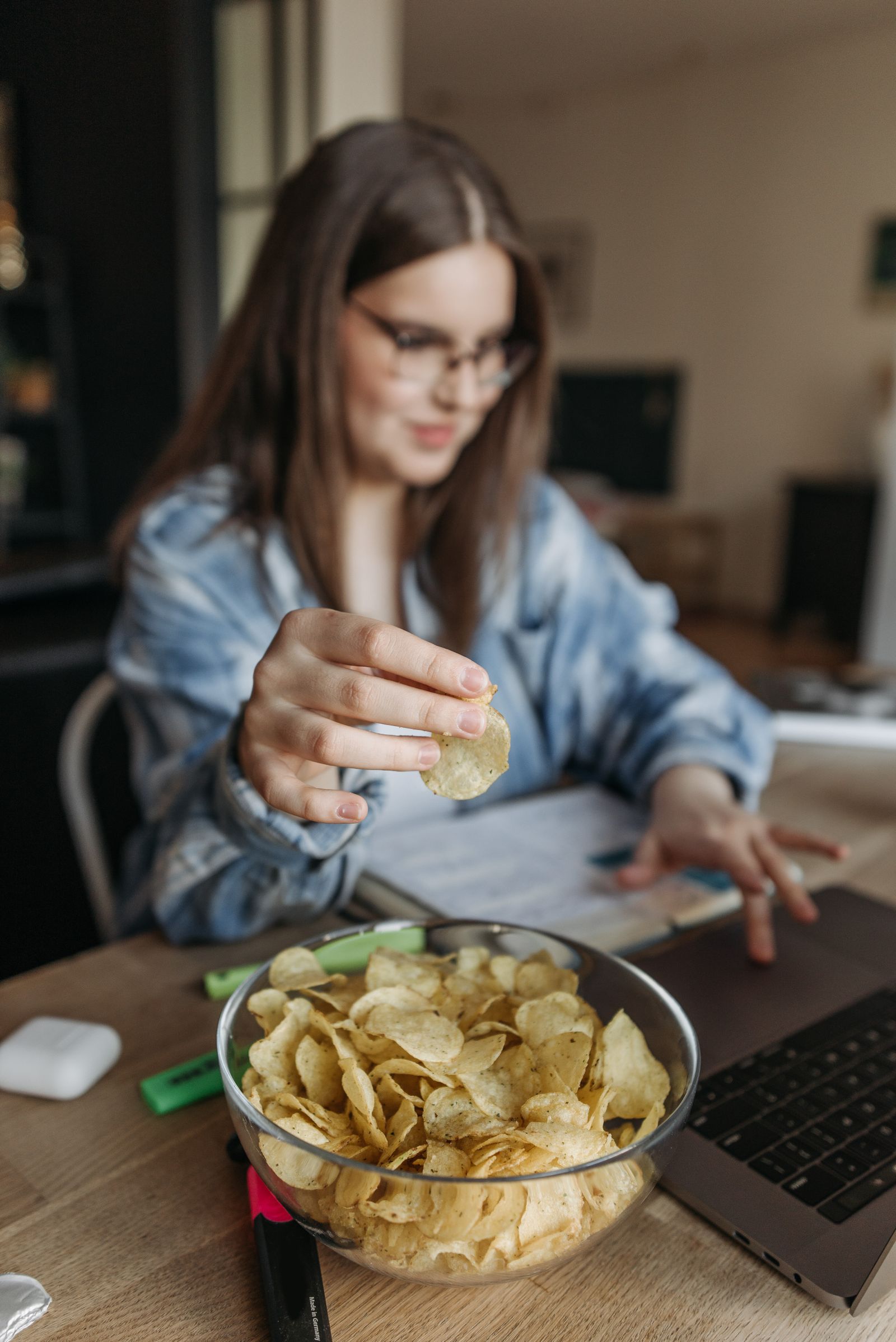 A woman snacking from a bowl of potato chips while working at a laptop