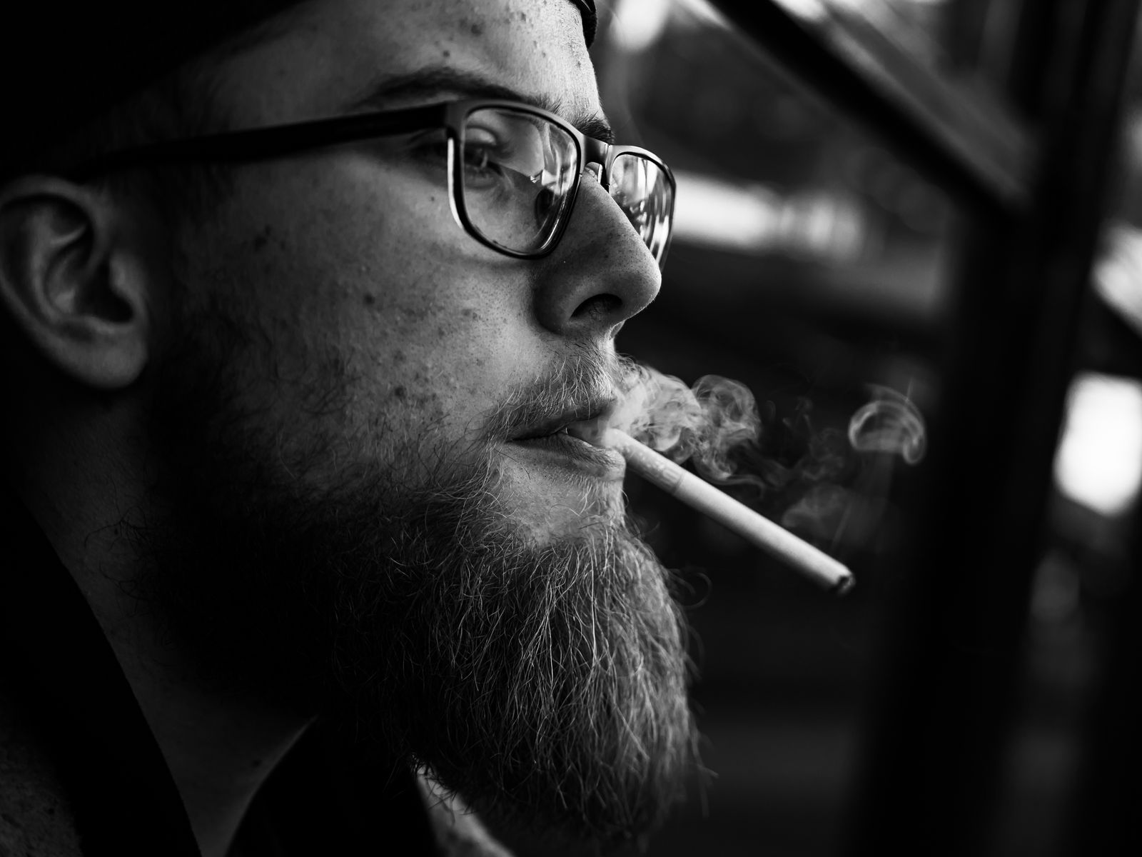 A bearded man with glasses smoking a cigarette